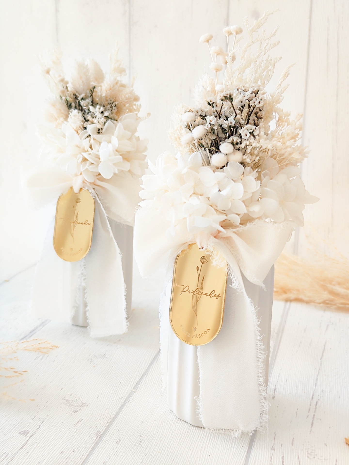 Duas velas decorativas brancas com flores secas e rótulos dourados