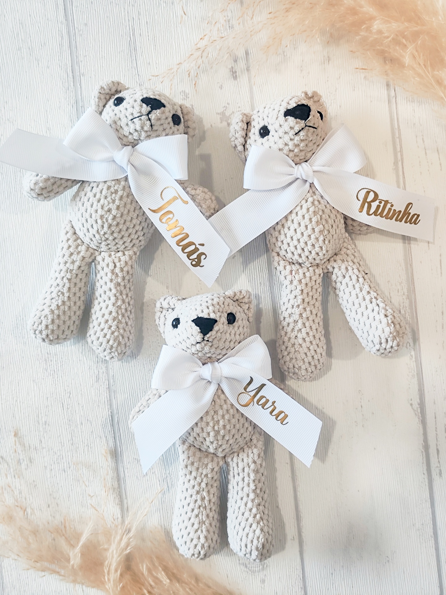 Três ursinhos de tecido bege claro com etiquetas de nomes e laços brancos