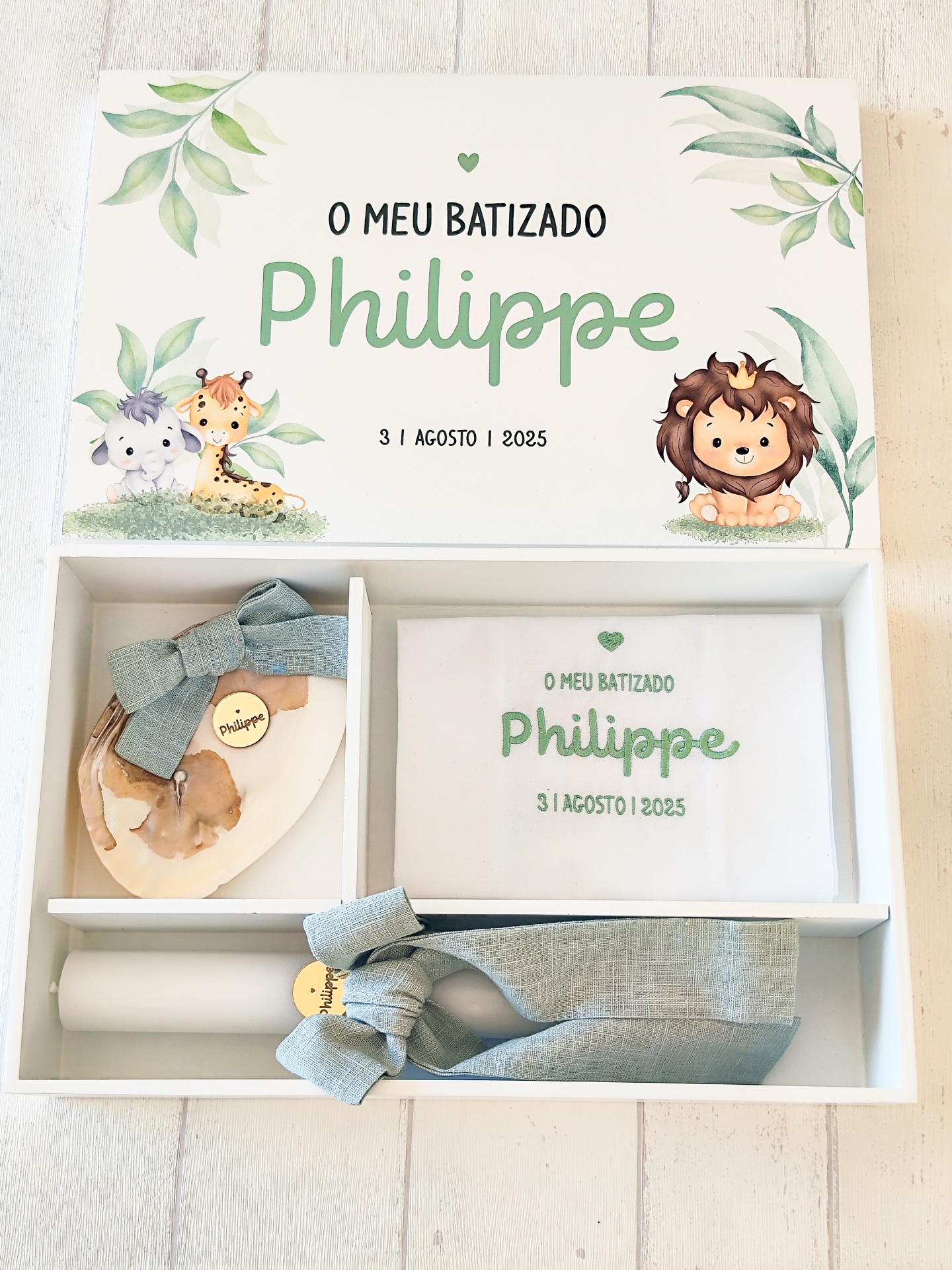 Caixa de batizado branca com texto e ilustrações de animais, contendo vela, coração de madeira e toalha bordada