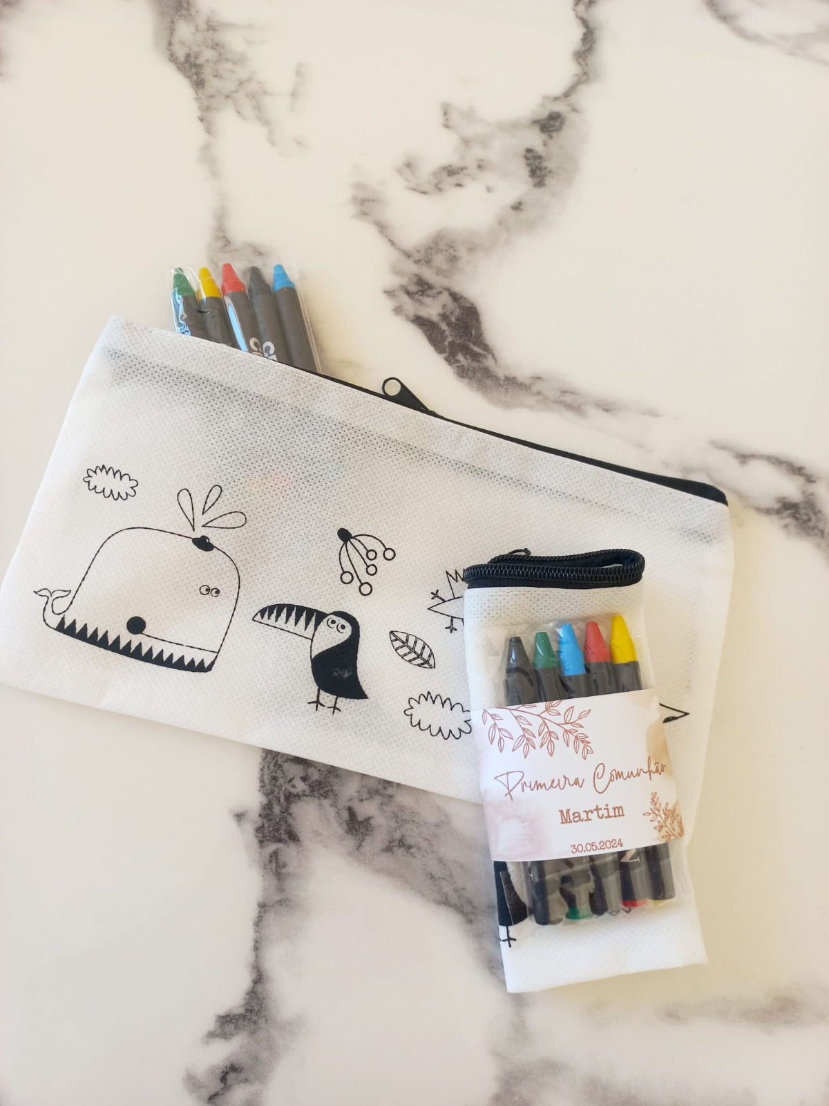 Estojo branco com ilustrações a preto e lápis de cor e embalagem com etiqueta de Primera Comunhão