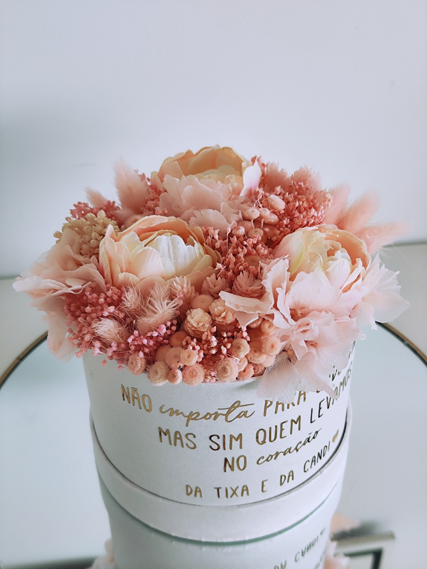 Arranjo floral artificial em caixa branca com texto dourado