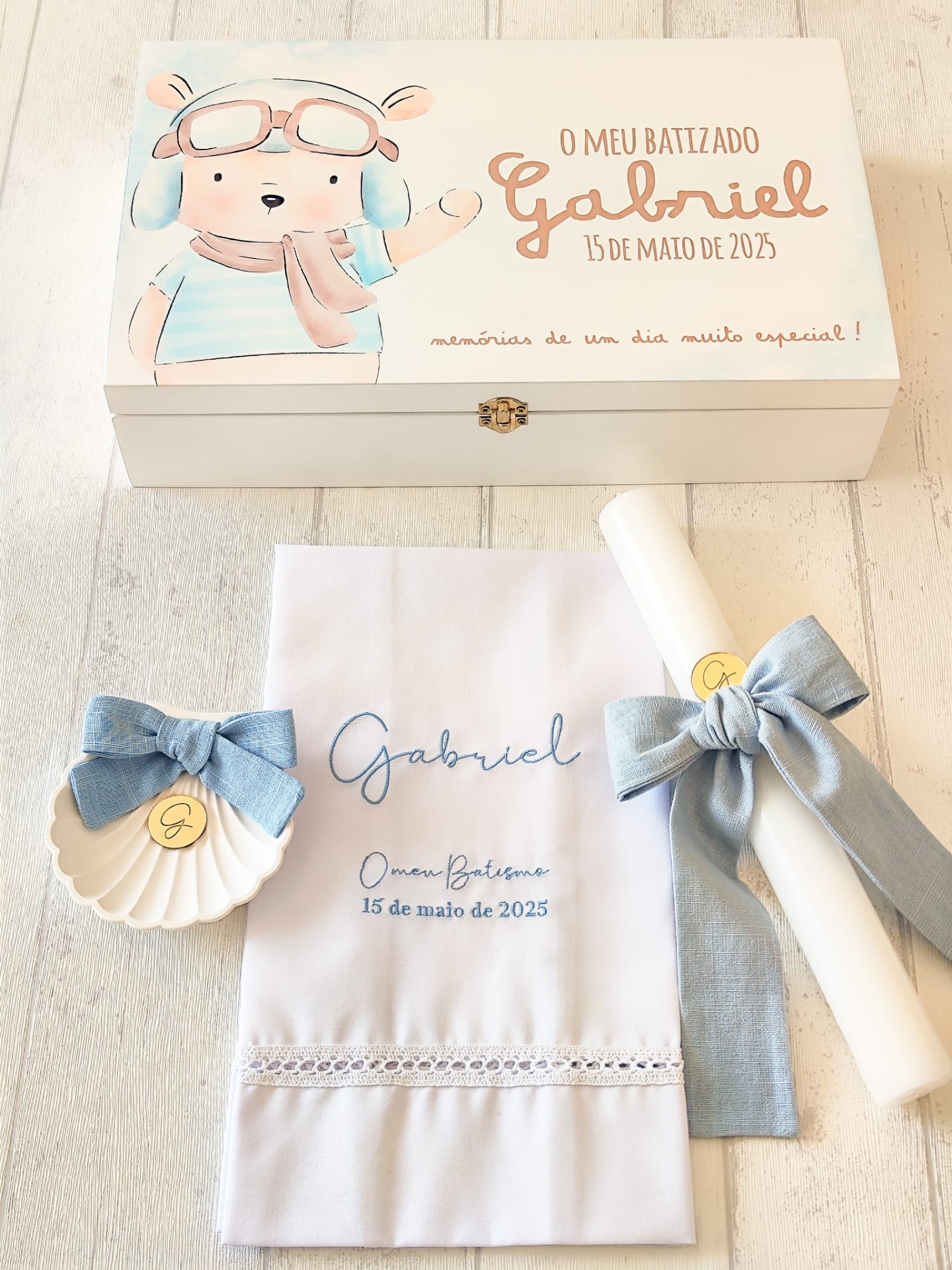 Conjunto de batizado com caixa de madeira decorativa, toalha branca bordada, vela com fita azul e concha com laço azul