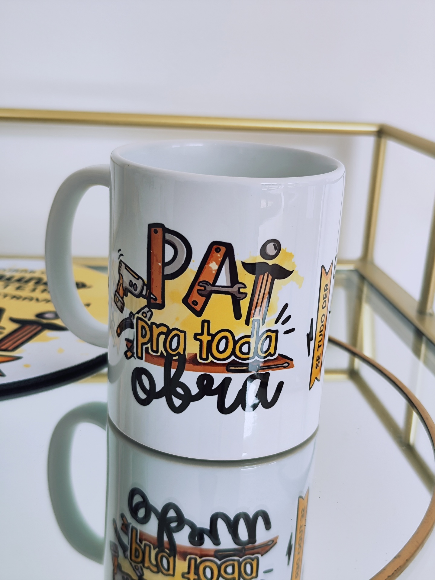 Caneca branca com texto colorido e asa sobre superfície espelhada