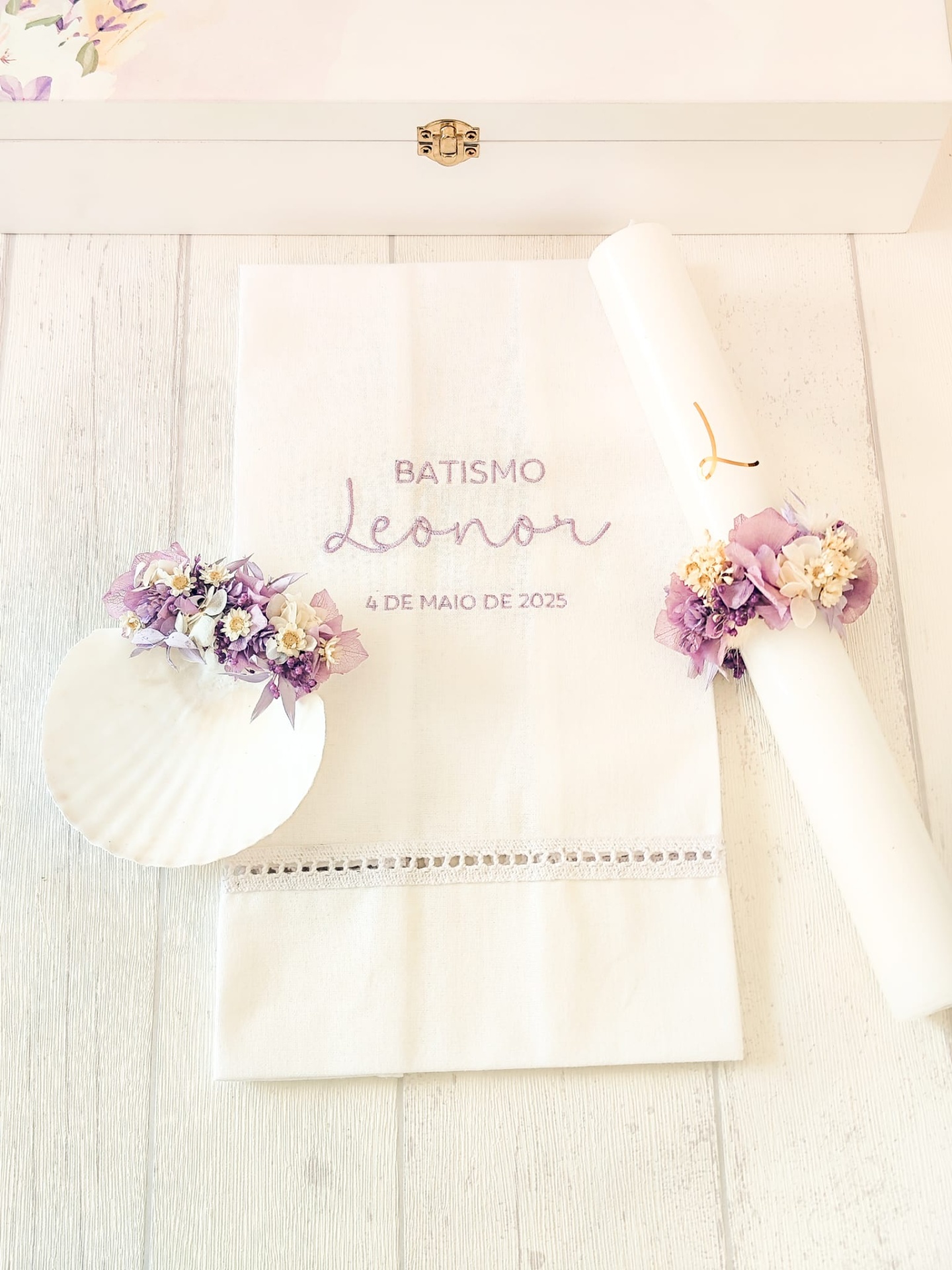 Conjunto de batismo com toalha bordada, vela decorada com flores e concha em fundo branco