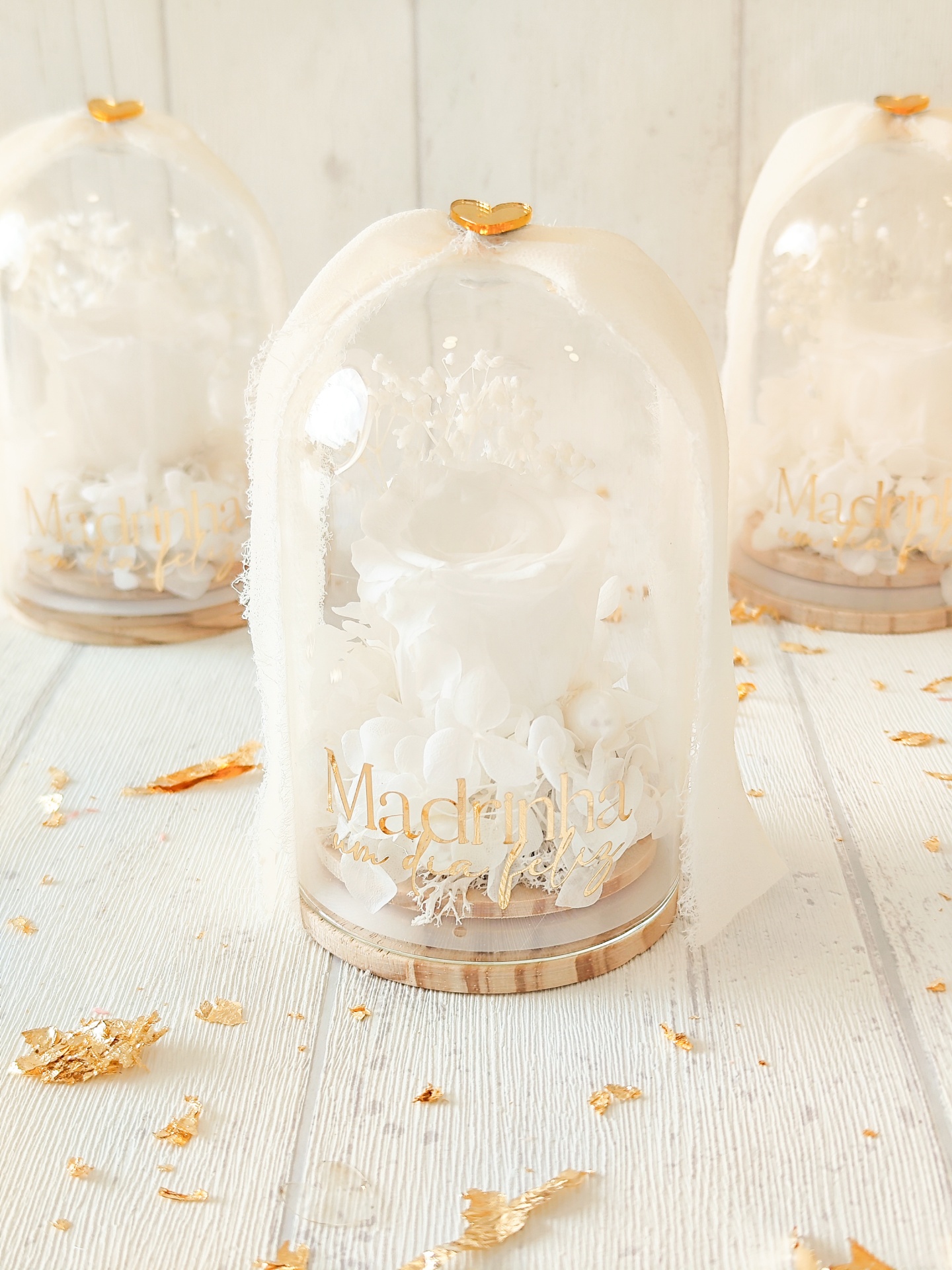 Arranjos florais em cúpulas de vidro com texto Madrinha um dia feliz e decoração branca e dourada