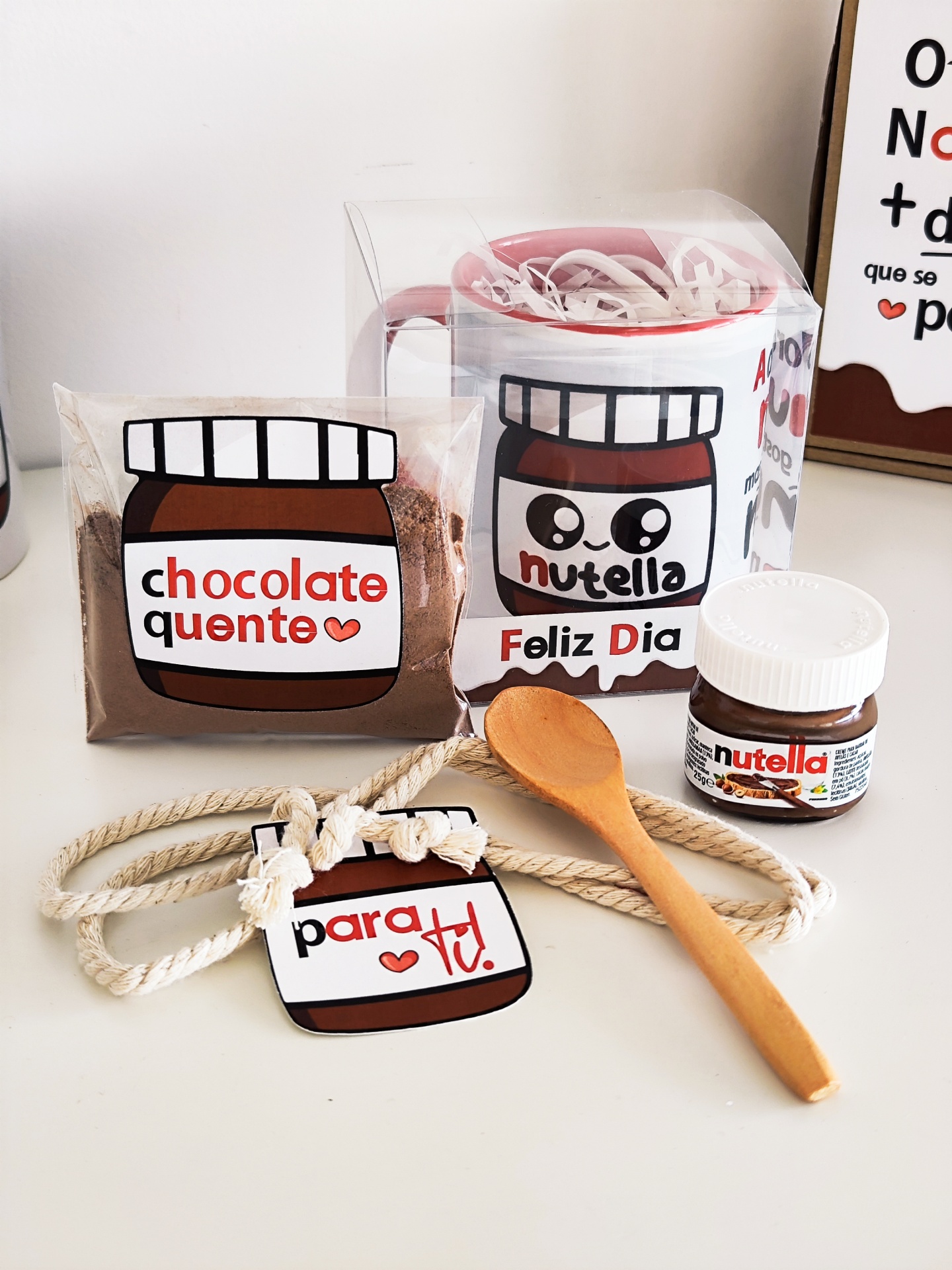Conjunto com caneca, cacau em pó, mini pote de Nutella, colher de madeira e cartão decorativo.