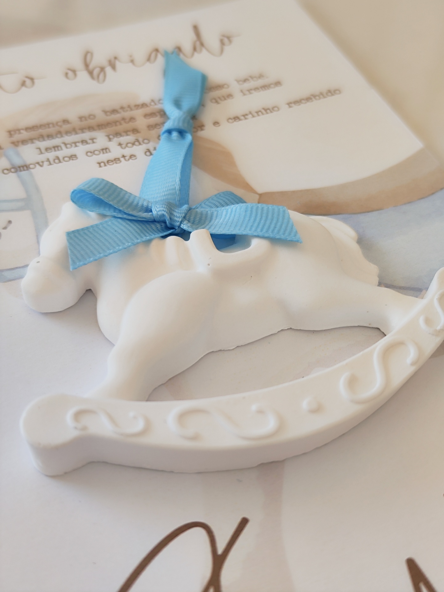 Cavalo de baloiço branco com laço azul sobre papel com texto em português