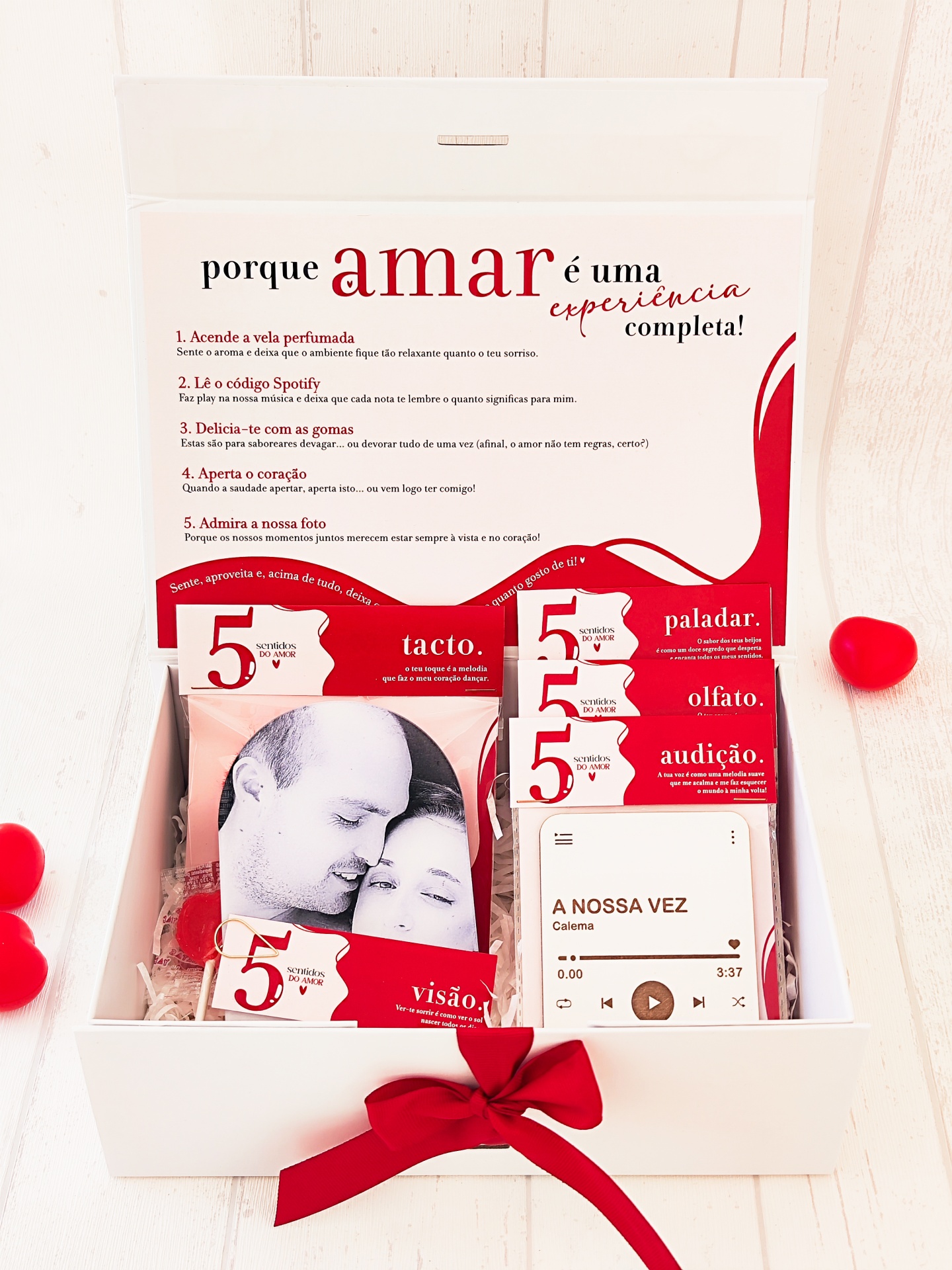 Caixa branca aberta com conteúdo temático sobre amor, com fichas vermelhas e brancas e laço vermelho.