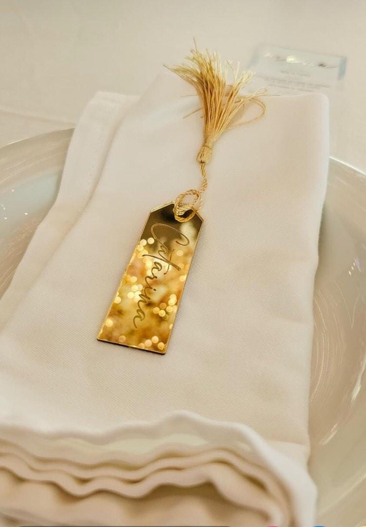 Marcador de mesa dourado com cacho dourado e nome Verónica sobre guardanapo branco em prato branco