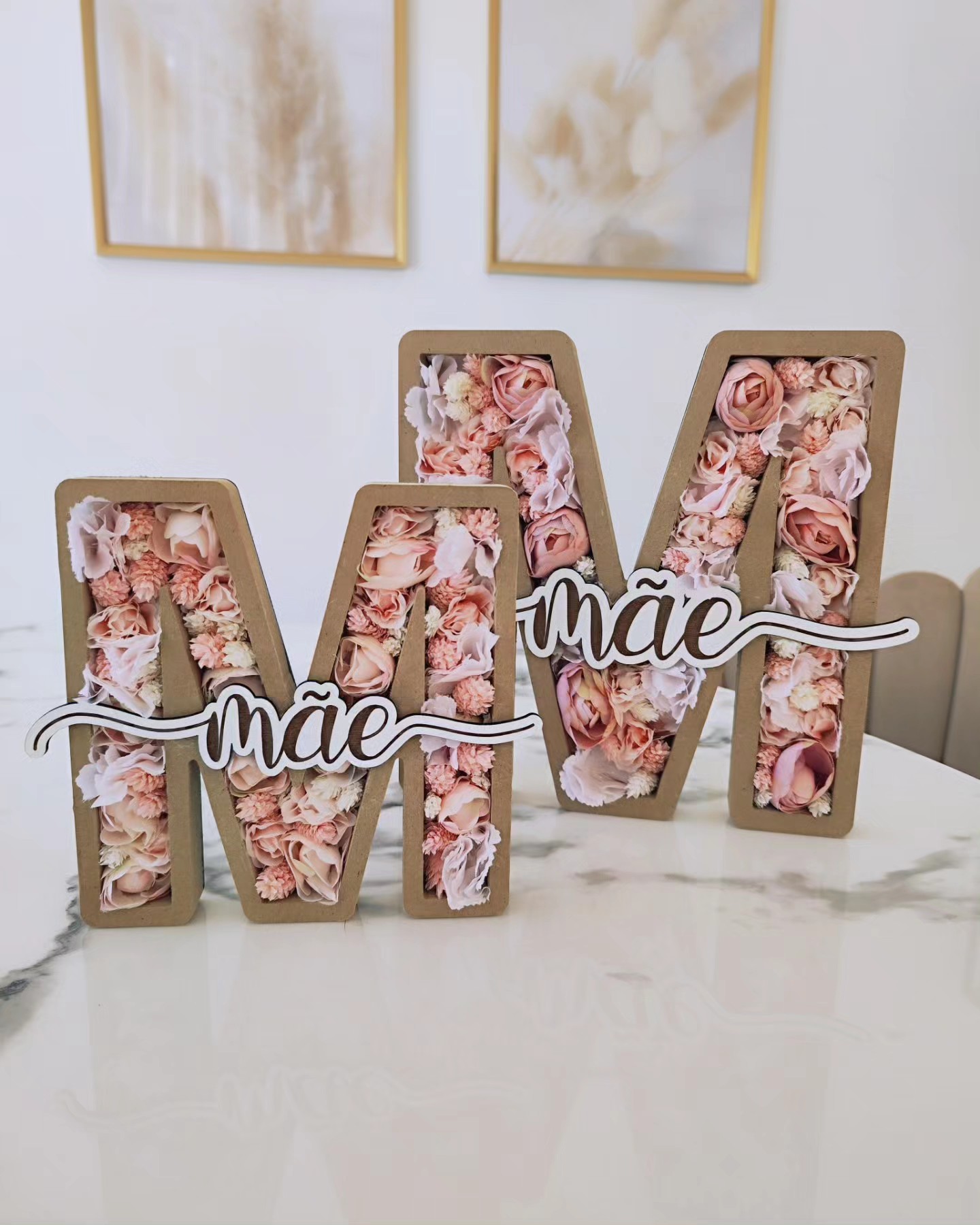 Duas letras decorativas M com flores artificiales rosa e bege e placa com 'mãe'