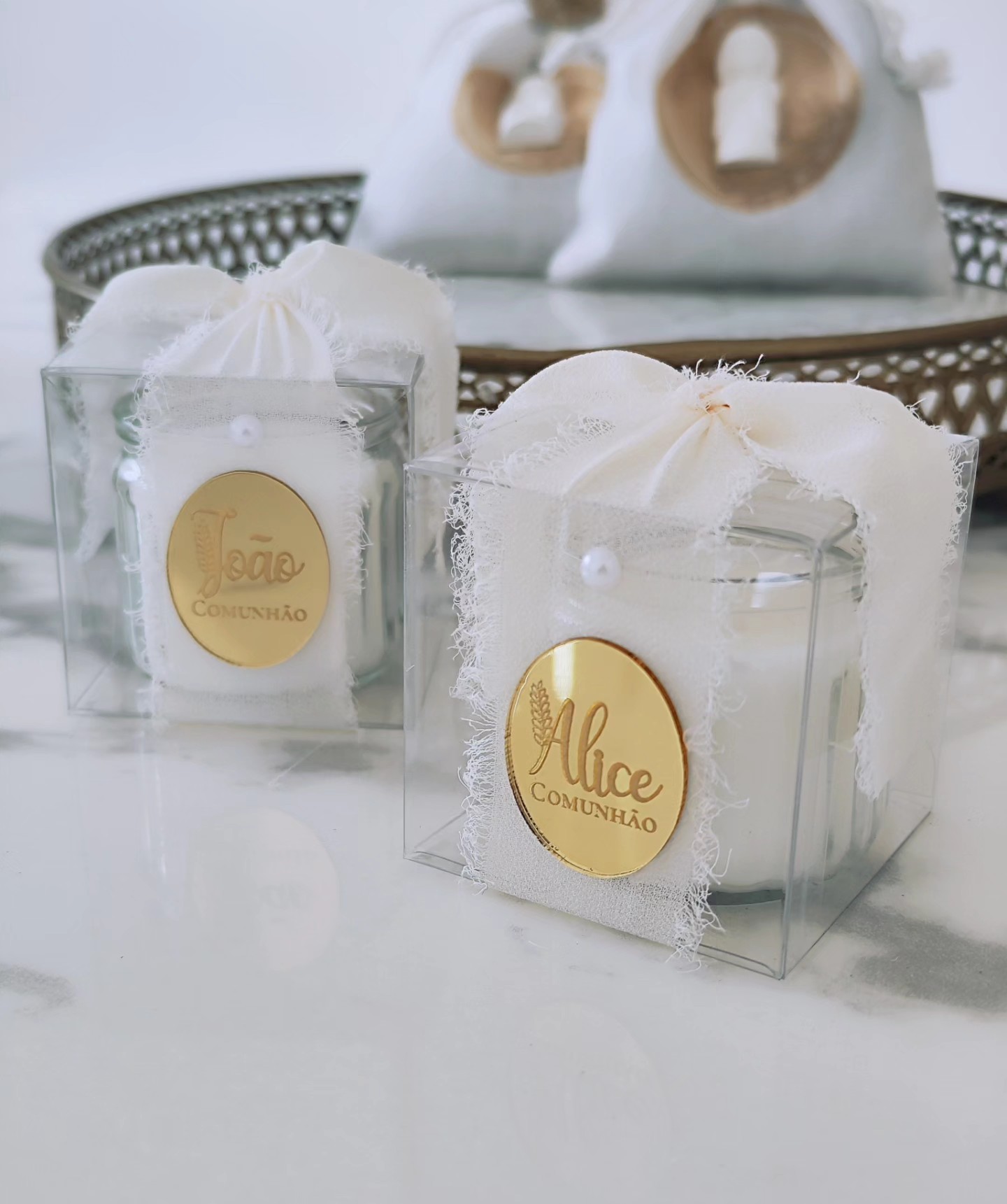 Caixa transparente com vela decorada, etiqueta dourada com nome Alice e João, palavra COMUNHÃO.