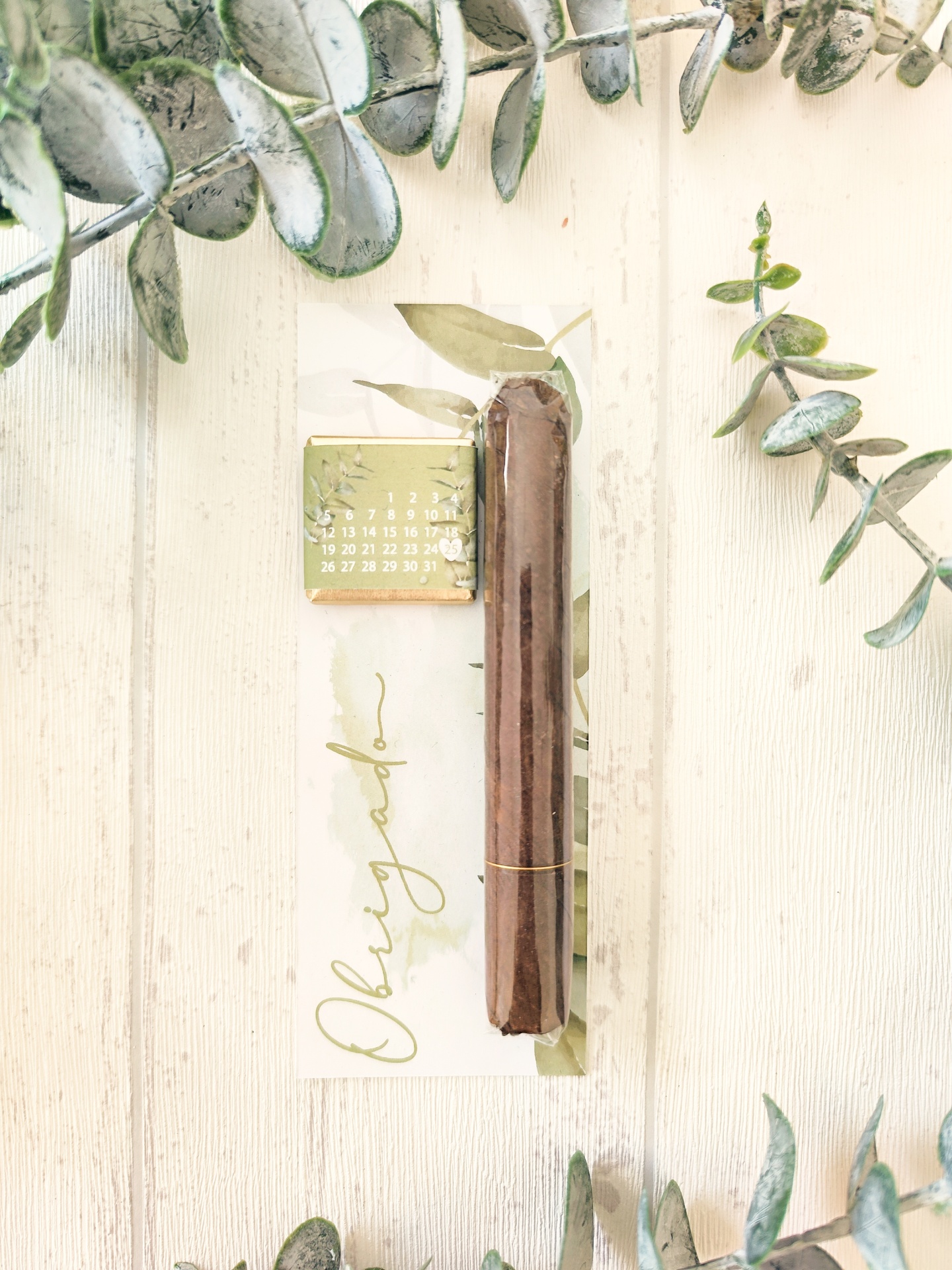 Vela castanha embalada e cartão com texto Obrigado e calendário pequeno em superfície de madeira com folhas decorativas