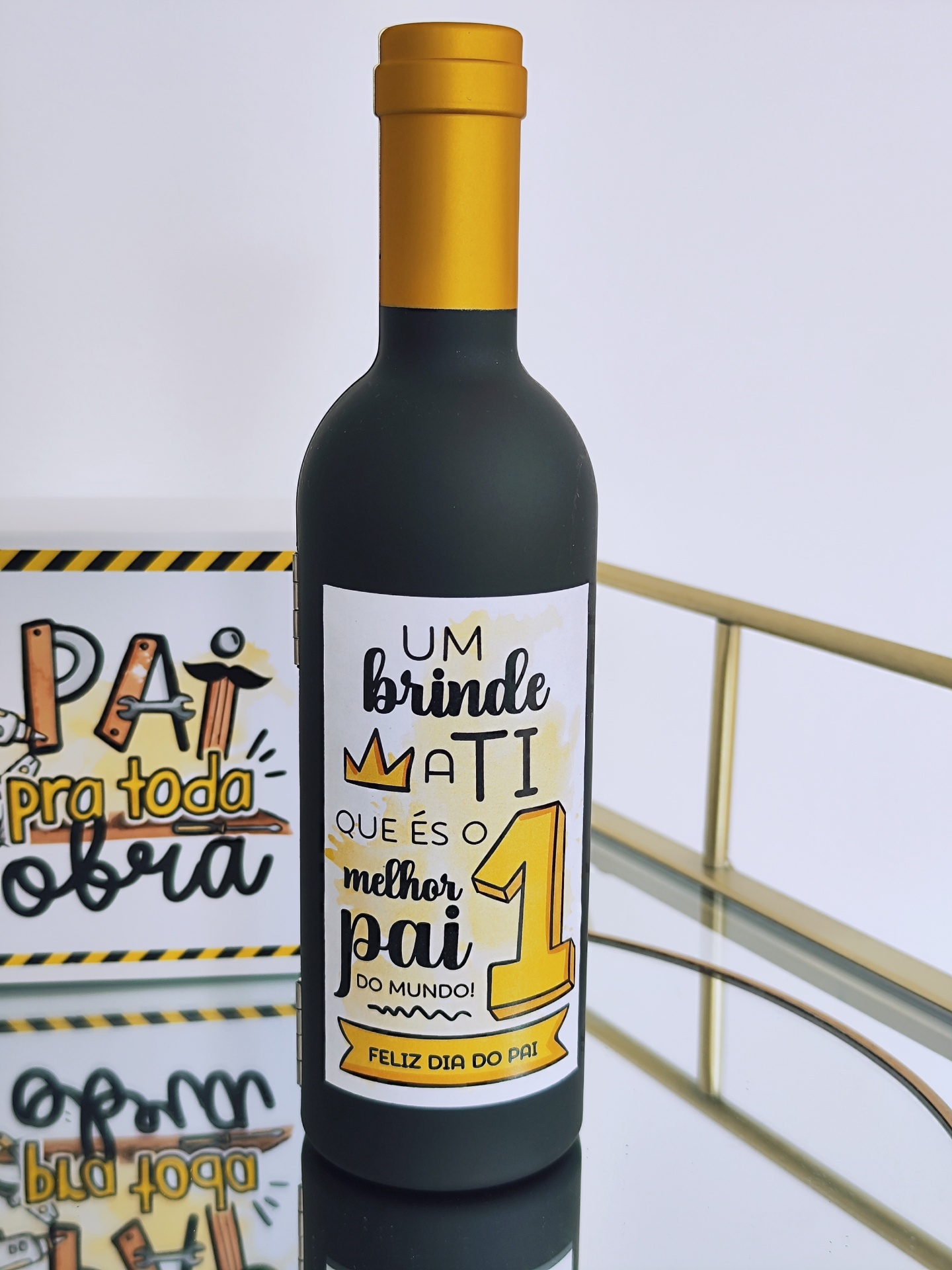 Garrafa com rótulo colorido e tampa dourada sobre superfície de vidro com placa decorativa ao fundo