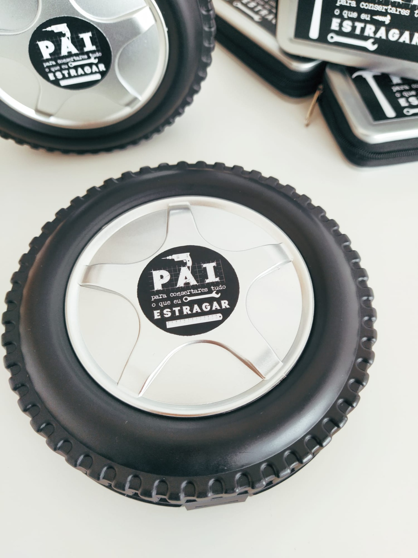 Produto em forma de roda com autocolante preto 'PAI para consertar tudo o que eu ESTRAGAR' em fundo branco