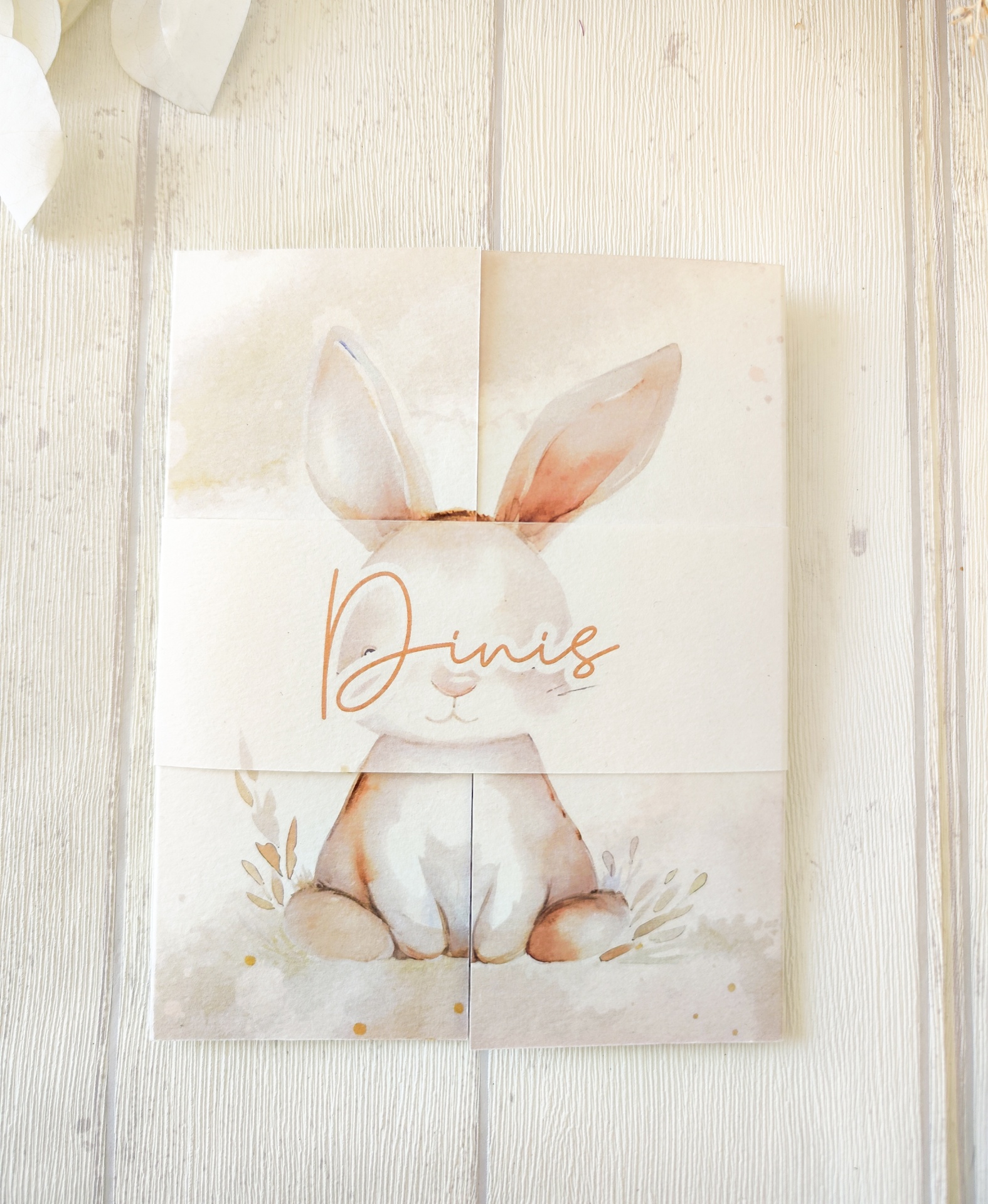Cartão com desenho de coelho e nome Dinis vez sobre fundo de madeira clara