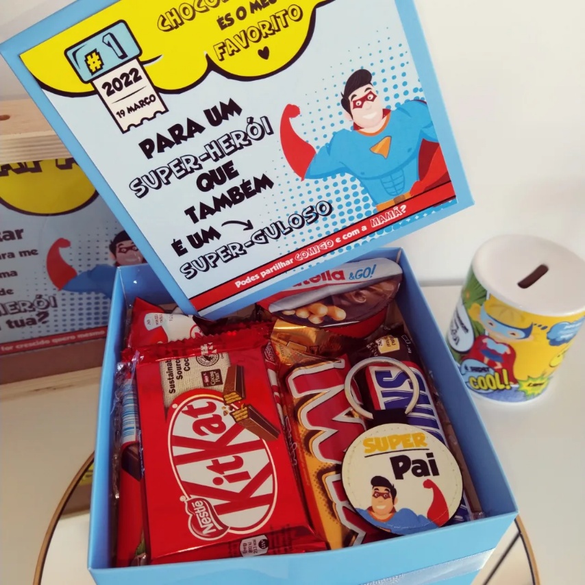 Caixa azul com chocolates Kit Kat, Twix e cookie, cartão com mensagem e cofrinho amarelo e branco