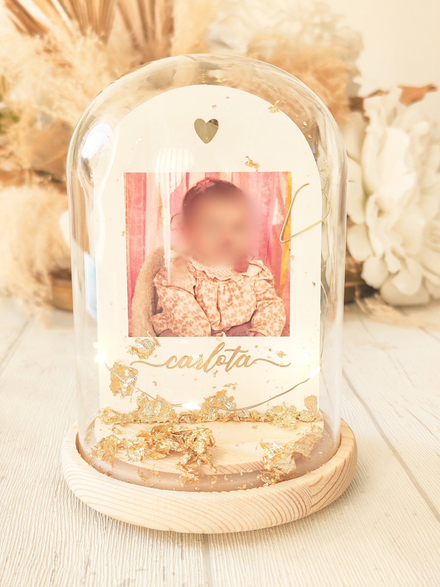 Objeto decorativo com foto de criança, base de madeira e cúpula de vidro com decoração dourada