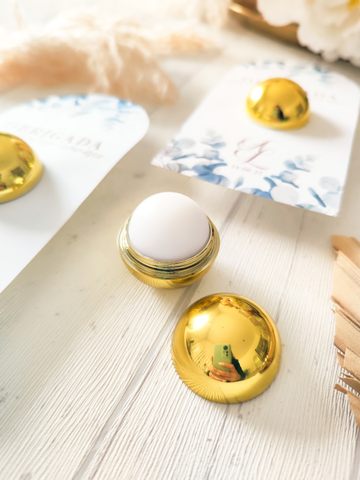 Bálsamo labial em embalagem dourada com cartão floral azul