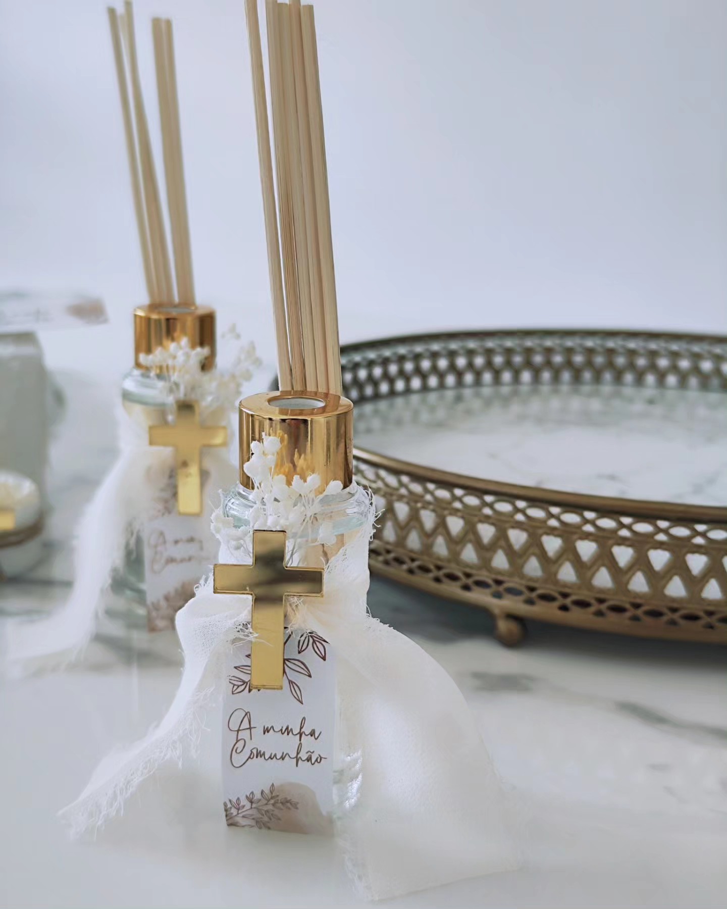 Difusores de ambiente com cruz dourada e tecido branco em superfície de mármore