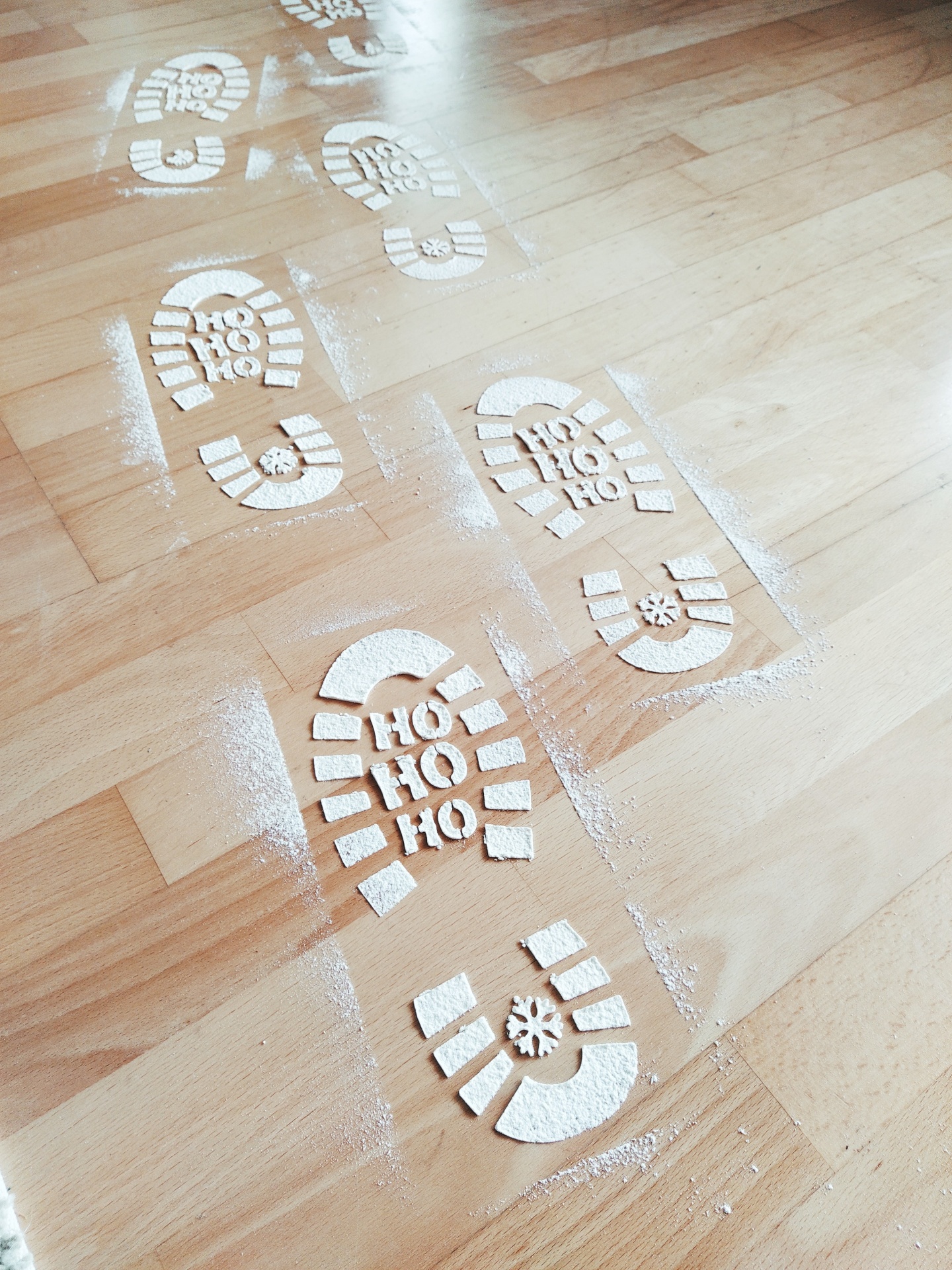 Pegadas de bota com texto HO HO HO e floco de neve em pó branco sobre chão de madeira