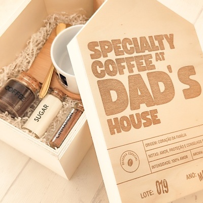 Caixa de madeira clara com tampa gravada e itens para café, incluindo frascos de vidro, chávena e colher