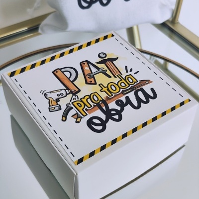 Caixa branca de cartão com tampa decorada com texto 'Pai pra toda obra' e desenhos de ferramentas