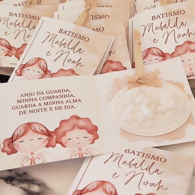 Convite de batismo com desenho de crianças e pendente decorativo branco em relevo de anjo com fita bege.