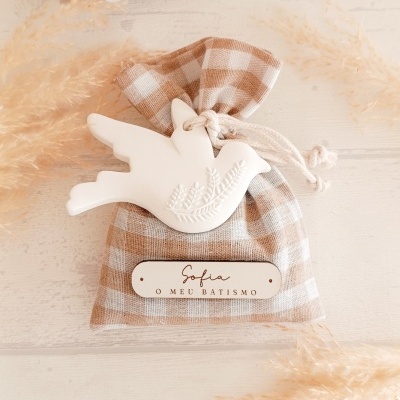 Saquinho de tecido xadrez castanho e branco com figura de pássaro branco e placa com texto de batismo