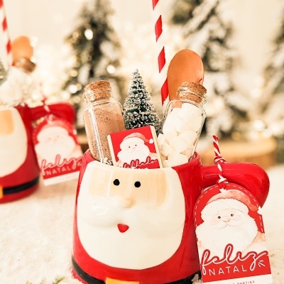 Caneca de Pai Natal recheada com ingredientes para chocolate quente e decoração natalícia.