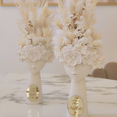 Vasos brancos em forma de cabeça com flores secas e placa dourada com texto 'you are magic'
