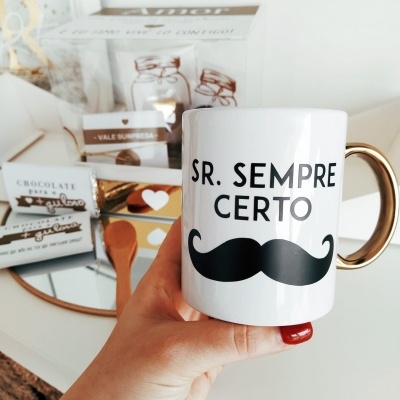 Caneca branca com texto e bigode, com fundo de embalagens de chocolate e oferta
