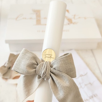 vela branca com laço cinzento e selo dourado, caixa branca ao fundo