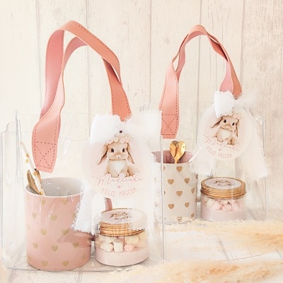 Conjuntos de presentes de Páscoa com canecas cor-de-rosa, frascos com marshmallows e sacos transparentes com alças cor-de-rosa e etiquetas de coelhinha.