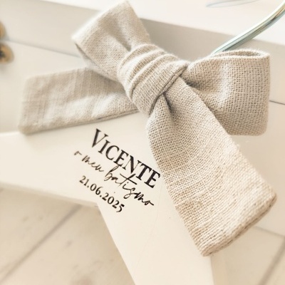 Cabide branco de madeira com laço bege e texto personalizado em preto.