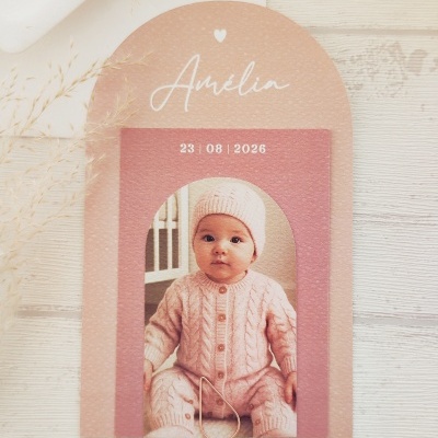 Convite de papel decorado com foto de bebé vestindo roupa rosa e texto Amélia 23 08 2026.