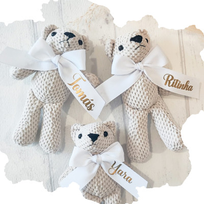 Três ursinhos de pelúcia bege com fitas brancas e nomes em dourado