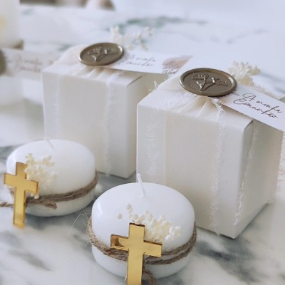 Velas brancas decoradas com cruz dourada e caixas embaladas brancas