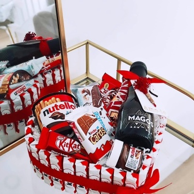 Cesta de presente com chocolates Kinder, Nutella, KitKat e garrafa de licor MAGOS sobre mesa espelhada