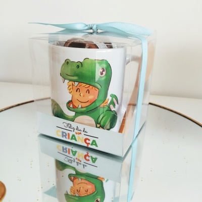 Caneca com ilustração de criança em fato de dinossauro embalada em caixa transparente com fita azul