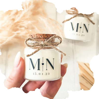 Frascos pequenos de vidro com velas brancas e tampas de cortiça com laços de corda natural, texto M N e data 15.04.23