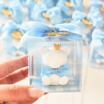 Figura de urso branco com coroa dourada e laço azul em caixa transparente com fita azul