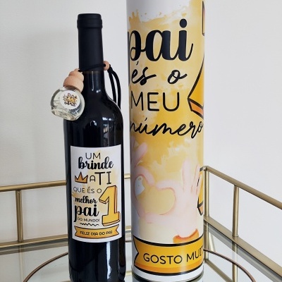 Garrafa de vinho com rótulo comemorativo para o Dia do Pai e embalagem cilíndrica ao lado, em mesa espelhada