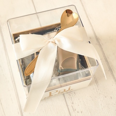 Embalagem de presente transparente com laço branco e colher dourada em fundo de madeira clara