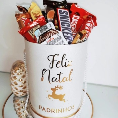 Recipiente branco com doces e decoração natalícia ao lado de objeto decorativo branco e dourado