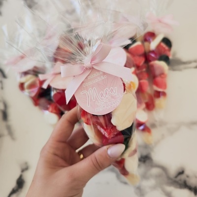 Cone transparente com doces coloridos, fita rosa e etiqueta rosa com texto, fundo marmoreado