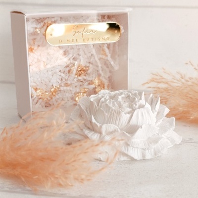 Flor decorativa branca em relevo com caixa branca de papel picado e placa dourada com texto