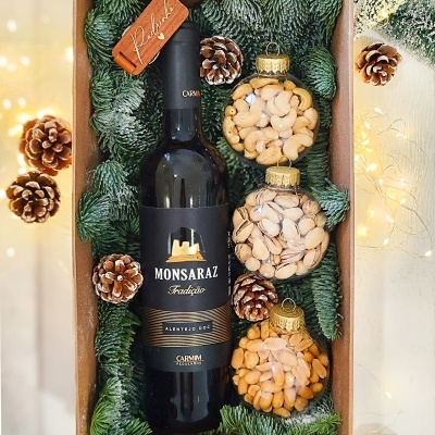 Conjunto de presente com garrafa de vinho e bolas decorativas de frutos secos em caixa com decoração de pinhas e ramos verdes