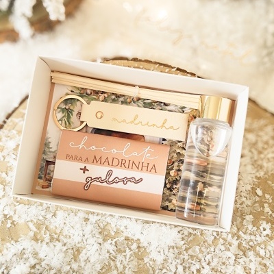 Conjunto presente com chocolate, chaveiro e frasco em caixa branca sobre superfície com neve artificial