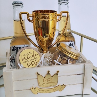 Cesta de madeira com duas garrafas de Corona, troféu dourado, frasco de amendoins e botão dourado com texto
