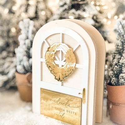 Porta decorativa branca com coroa dourada e placa com texto em cenário de Natal